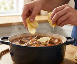 Un cuisinier ajoute des rondelles de pomme de terre et presse du citron dans une cocotte fumante pour réduire le sel.