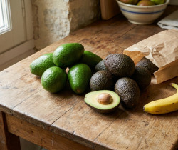Avocats verts et mûrs, un sac en papier et une banane sur une table en bois rustique.