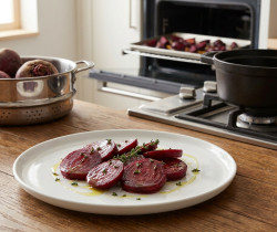 Assiette de rondelles de betteraves rôties avec du thym sur une table en bois, devant une cuisine équipée.