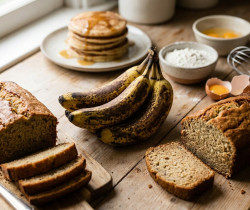Bananes mûres posées sur une table en bois avec du pain à la banane et des pancakes, accompagnés d'ingrédients de cuisine.