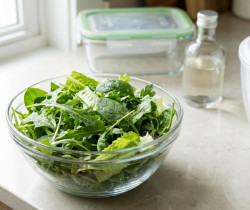 Bol de salade fraîche posé sur un comptoir de cuisine avec une essoreuse à salade et une boîte de conservation en arrière.